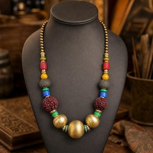 Bold multicolor carved bead and brushed gold sphere necklace worn with an ivory linen top in warm natural window light