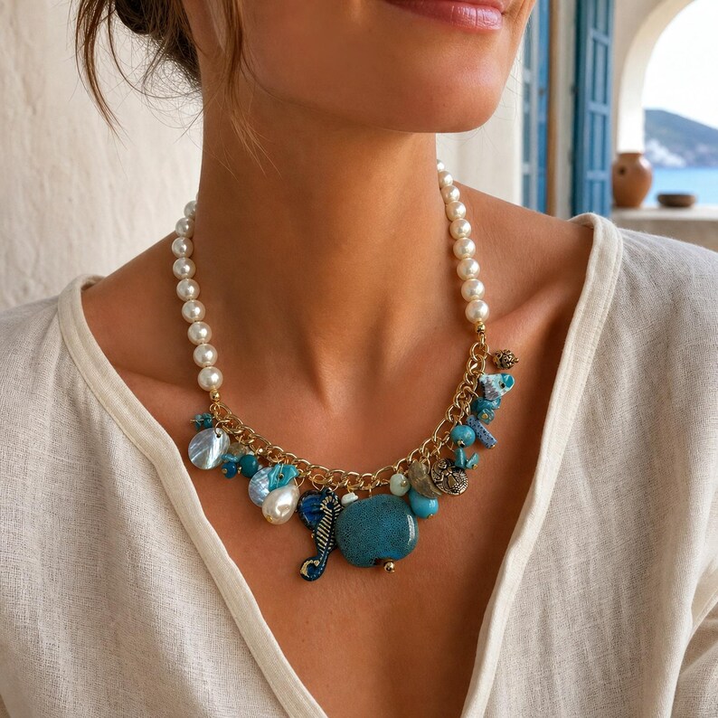 May include: A necklace featuring a strand of white pearls connected to a gold-tone chain. The chain is adorned with various charms, including blue ceramic pieces, a seahorse, and iridescent shell-like beads, creating a coastal-inspired design.