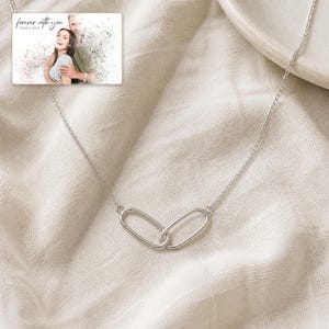 May include: A silver-toned necklace featuring two interlocking oval links as a central pendant. A small rectangular card is included, displaying a printed photograph of a couple and the text "forever with you" in a cursive script font.
