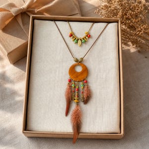 May include: A two-piece necklace set featuring a short beaded chain with small green, red, and gold-toned leaf charms, and a longer cord necklace with a large wooden circle pendant, colorful beads, and three brown feathers hanging from the base.