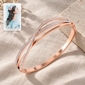 Crossover Bangle Bracelet, laid on fabric. A sample personalized digital greeting card is shown alongside.