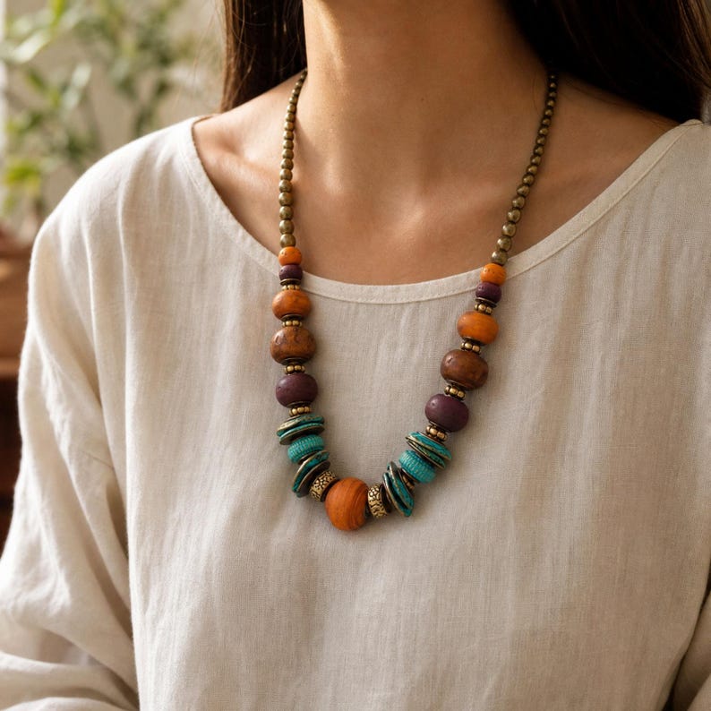 May include: A beaded necklace featuring a mix of round and disc-shaped beads in shades of orange, purple, and turquoise, interspersed with small metallic bronze-toned spacer beads and a chain of small bronze-toned beads leading to the clasp.
