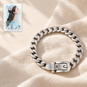 Closed silver tone belt buckle bracelet in an oval on folded ivory linen, with smooth pointed tab beneath keeper. A personalized digital greeting card is shown alongside.