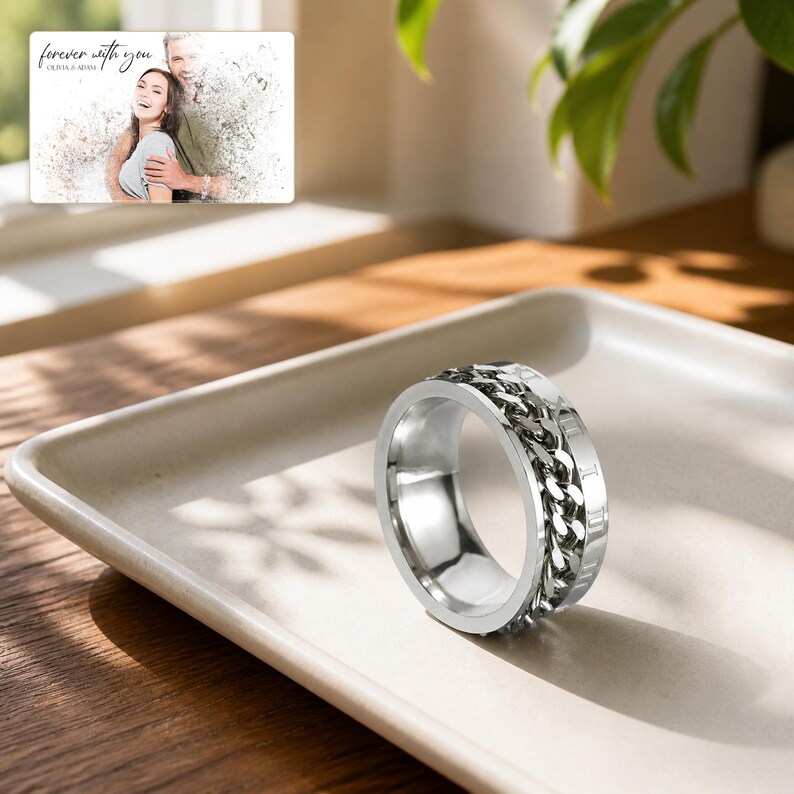 May include: A silver-toned metal spinner ring featuring a central rotating chain link band flanked by smooth edges. The ring is displayed alongside a rectangular card showing a photograph of a couple with the text "forever with you OLIVIA & ADAM".