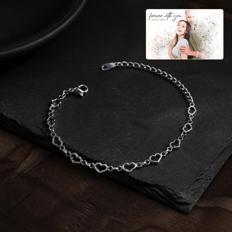 May include: A silver-toned chain bracelet featuring a series of interconnected open heart-shaped links. In the upper right corner, a rectangular card displays a black and white photograph of a couple with the text "forever with you" and "OLIVIA & ADAM".