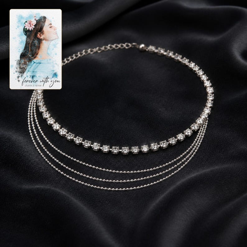 May include: A silver-toned multi-strand necklace featuring one row of clear square-cut rhinestones and three delicate beaded chains. Included is a small rectangular card with a watercolour illustration of a person and the text forever with you.
