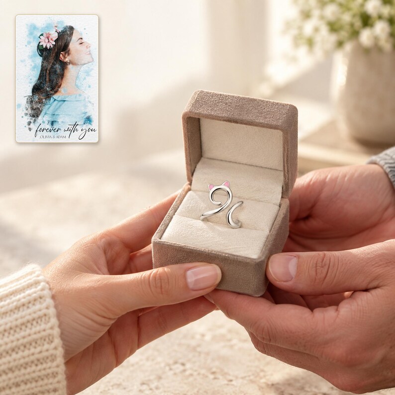 Two adults exchange an open taupe styling box containing one silver-tone cat-curl ring. A personalized digital greeting card is shown alongside.
