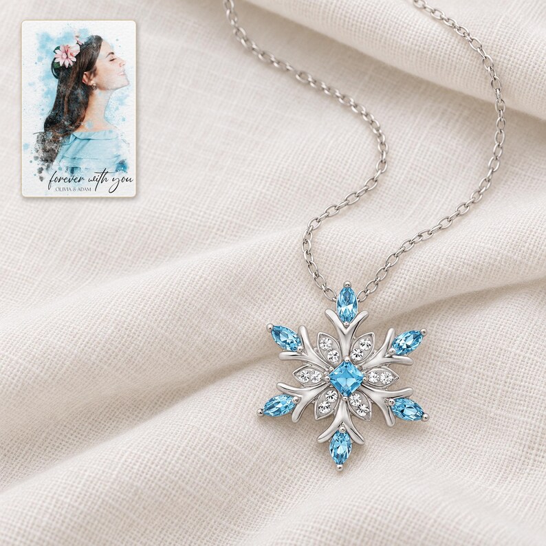 Winter Azure Snowflake Necklace arranged on soft ivory linen in a refined neutral flat lay. A personalized digital greeting card is shown alongside.