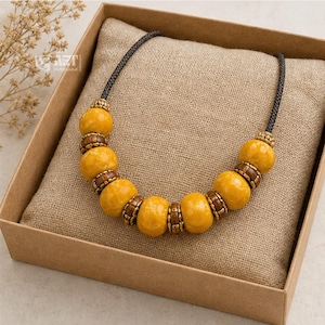Flatlay lifestyle photo of mustard yellow beaded boho statement necklace styled on linen and natural stone