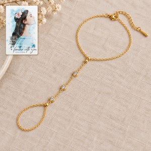 Golden Three stone style Hand Chain arranged on soft ivory linen in a refined neutral flat lay. A personalized digital greeting card is shown alongside.