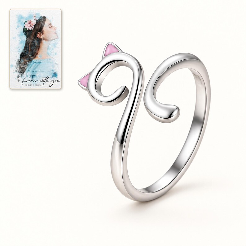 Single open cat-curl ring on an ivory-white background, showing the two soft pink ears and curved tail. A personalized digital greeting card is shown alongside.