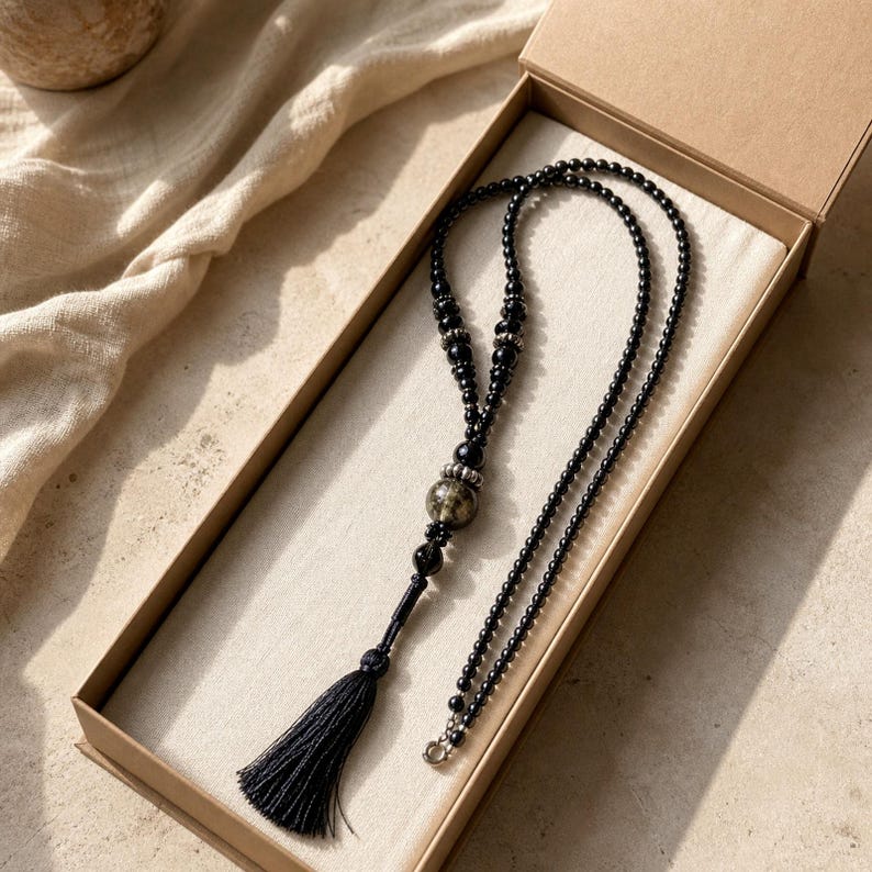 Long black beaded necklace with smoky metallic orb black teardrop accents and long tassel worn with an ivory linen top in warm natural window light
