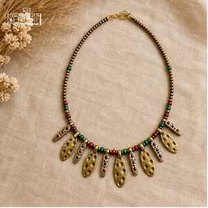 May include: A necklace featuring a series of small metallic beads in a bronze tone, interspersed with alternating red and green spherical beads. The piece includes several dangling, textured, oval-shaped metallic charms with small red and green accents.