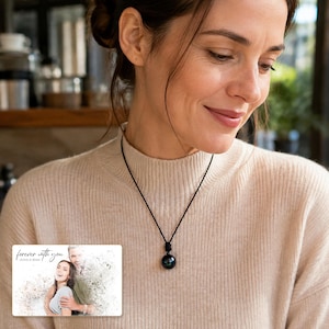 Black cord necklace with a dark round pendant, adult lifestyle view. A personalized greeting-card example appears in the corner.