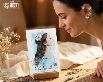 May include: A watercolor portrait on a wooden stand, featuring a woman with a flower in her hair, the text "forever with you" and the names Olivia & Adam. The image is on a wooden table with flowers.