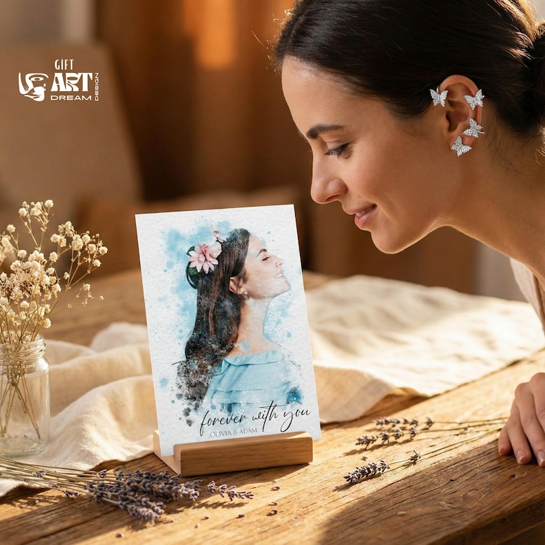 May include: A watercolour portrait on a wooden stand, featuring a woman with a flower in her hair, the text "forever with you" and the names Olivia & Adam. The image is on a wooden table with flowers.