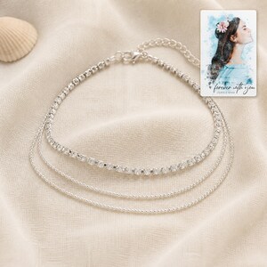 May include: A silver-toned multi-strand anklet featuring one row of clear rhinestones and two delicate beaded chains. Included is a rectangular card with a watercolour illustration of a person and the text "forever with you OLIVIA & ADAM".
