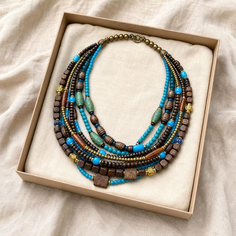 May include: A multi-strand statement necklace featuring a combination of dark brown wooden cube and cylindrical beads, bright turquoise round beads, and metallic gold-toned accents. The design includes patterned green beads and a toggle clasp closure.