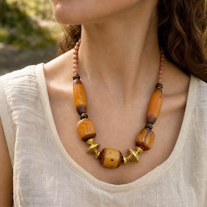 Brown and gold statement beaded necklace displayed on a jewelry bust with the layered beadwork and pendants visible