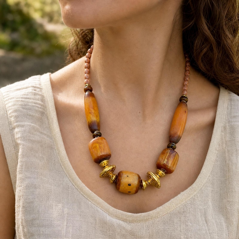 Brown and gold statement beaded necklace displayed on a jewelry bust with the layered beadwork and pendants visible