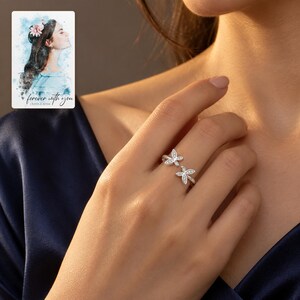 Adult woman wearing the double butterfly open ring with a navy satin outfit in evening light. A personalized digital greeting card is shown alongside.