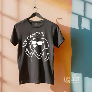 May include: Black t-shirt with a white graphic of a dog wearing sunglasses and giving the middle finger. The text "Hey Cancer!" is above the dog.