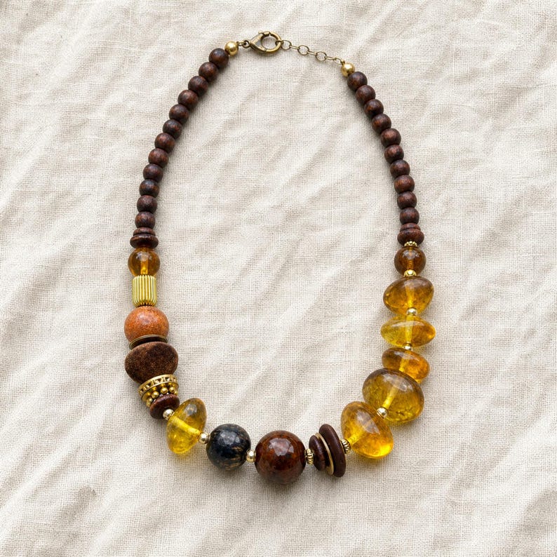 Gift ready presentation of Asymmetric honey amber and dark brown single strand statement beaded necklace in an open jewelry box lined with natural ivory linen