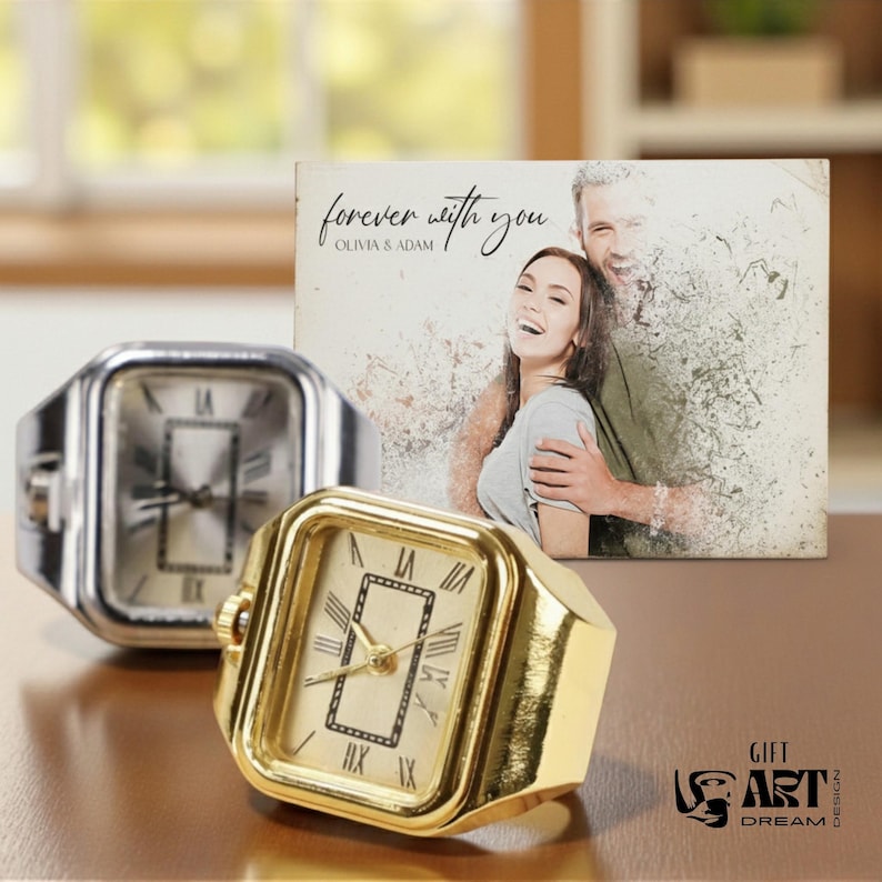 May include: Two square-faced ring watches, one silver and one gold, with Roman numeral hour markers. A photo with the text "forever with you" and a couple is in the background. The watches are on a brown surface.
