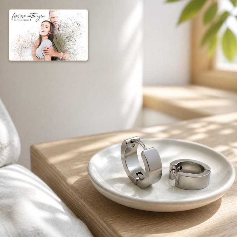 May include: A pair of silver-toned hoop earrings with a smooth, polished finish resting on a small white ceramic dish. Above the dish, a rectangular card displays a photograph of a couple with the text "forever with you" and "OLIVIA & ADAM".