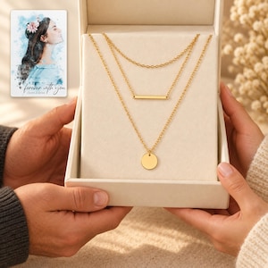 Two adults holding an open presentation box with all three gold-tone necklaces visible on a cream insert. A personalized digital greeting card is shown alongside.