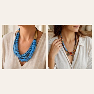 May include: A multi-strand necklace featuring bright blue beads and a textured gold-tone metal accent piece, alongside a second necklace with blue and orange beads, small metal charms, and a dark cord, both worn over a light beige linen shirt.