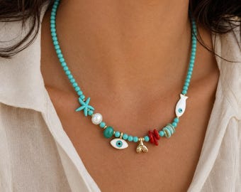 May include: A beaded necklace featuring small turquoise-colored beads interspersed with charms including a blue starfish, a white pearl, a white fish with an eye, a gold-toned mermaid tail, a red coral-like piece, and a white evil eye charm.