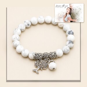 White and gray bead bracelet with silver-tone tree and hanging bead details, framed product view. A personalized greeting-card example appears in the corner.
