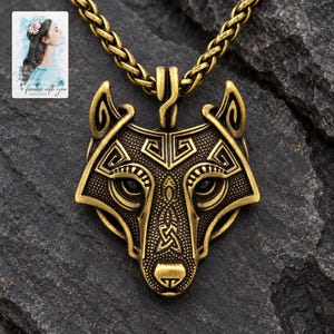 May include: A brass-toned metal pendant shaped like a wolf head with intricate geometric and knotwork engravings, suspended from a matching wheat chain. A small rectangular card featuring a watercolor illustration of a person and the text "forever with you" is visible in the upper left corner.