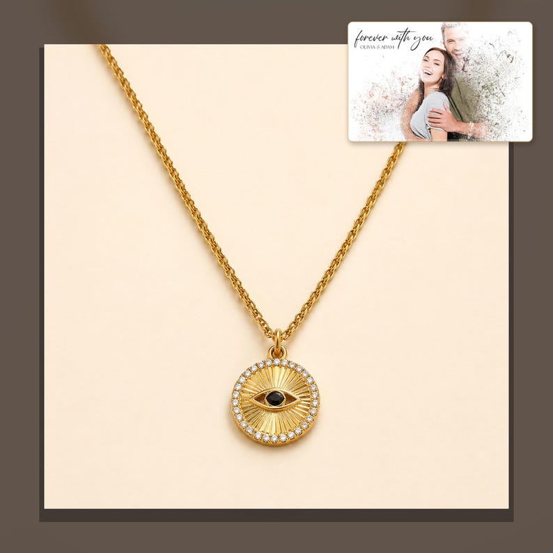 Gold-tone necklace with a round sunburst and black eye detail, alternate framed view. A personalized greeting-card example appears in the corner.