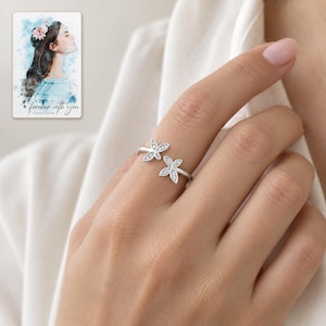 Adult woman wearing the delicate double butterfly open ring with its clear-accent wings facing the camera. A personalized digital greeting card is shown alongside.