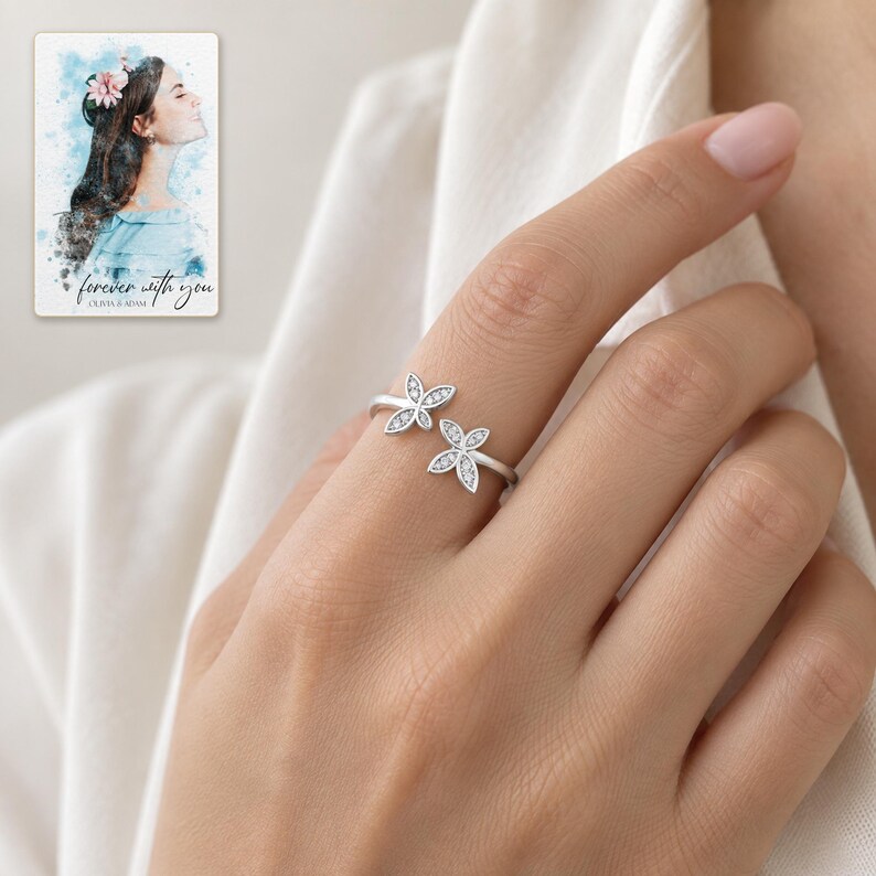 Adult woman wearing the delicate double butterfly open ring with its clear-accent wings facing the camera. A personalized digital greeting card is shown alongside.