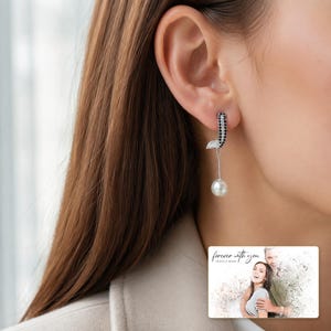 Silver-tone curved drop earrings with black accents and white round drops, worn view. A personalized greeting-card example appears in the corner.