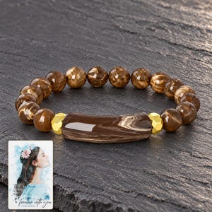 Cocoa Swirl Bar Bracelet styled against a dark luxury surface with the exact product finish clearly visible. A personalized digital greeting card is shown alongside.