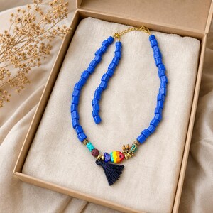 Puede incluir: Un collar que presenta una hilera de cuentas cil&iacute;ndricas de color azul brillante, acentuado con un peque&ntilde;o dije de pez multicolor, una cuenta texturizada de color marr&oacute;n oscuro, una cuenta turquesa y una borla azul oscuro con cierre dorado.
