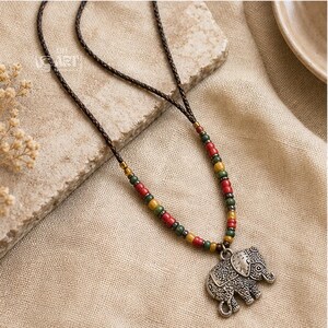 On-model lifestyle photo of long silver tone elephant pendant boho necklace worn with neutral clothing