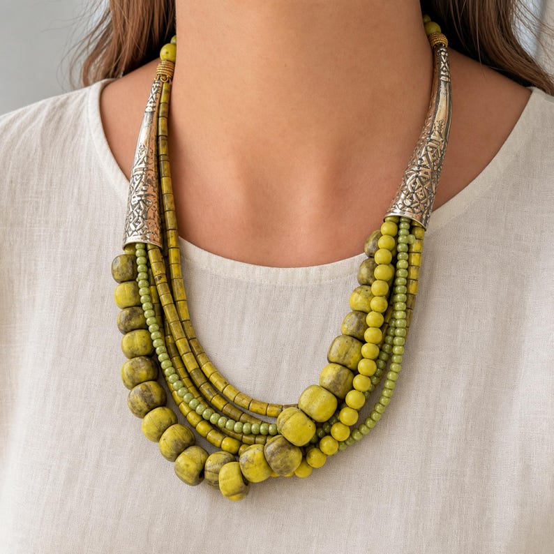 Pu&ograve; includere: Una collana a pi&ugrave; fili con perline di varie dimensioni e forme in tonalit&agrave; verde chartreuse e oliva. I fili sono uniti su ciascun lato da un componente conico in metallo color argento con un intricato motivo inciso.