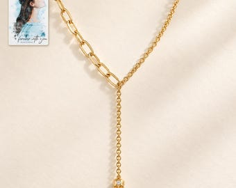 May include: A gold-toned necklace featuring an asymmetrical design with a thick oval link chain on one side and a delicate cable chain on the other. A central vertical drop chain ends in a small gold skull charm with a single embedded clear stone.