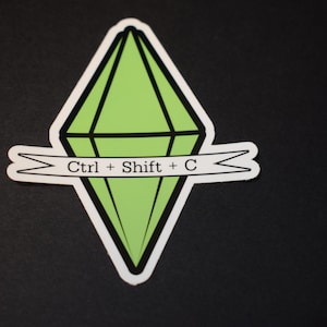 May include: A sticker featuring a green diamond shape with black outlines, a white border, and a banner that reads "Ctrl + Shift + C". The sticker is on a black background.
