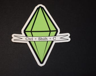 May include: A sticker featuring a green diamond shape with black outlines, a white border, and a banner that reads "Ctrl + Shift + C". The sticker is on a black background.
