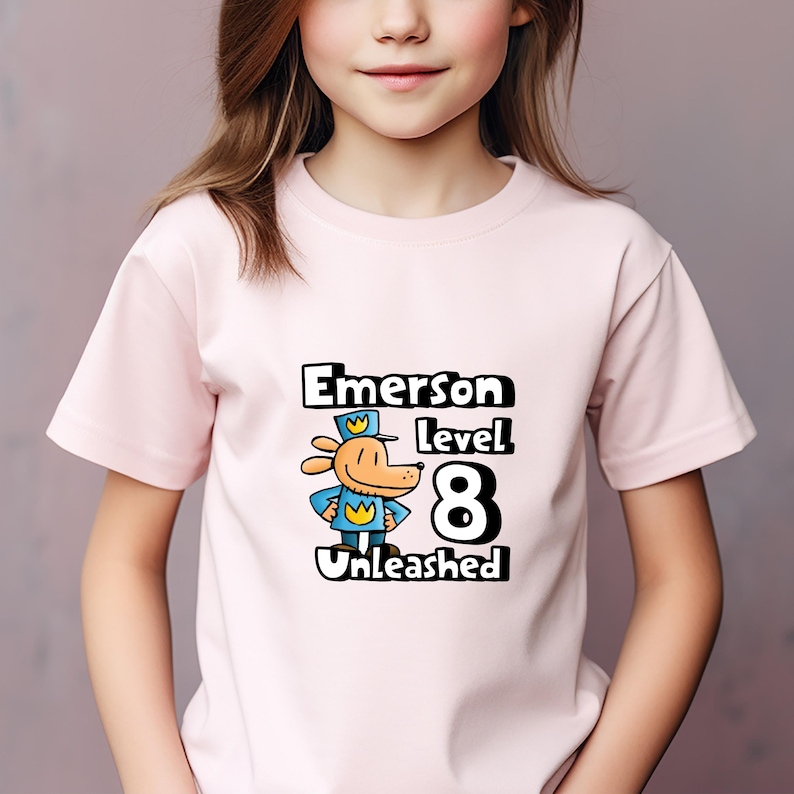 May include: Pink t-shirt with a cartoon dog wearing a blue uniform and a yellow crown. The text "Emerson Level 8 Unleashed" is printed on the shirt.