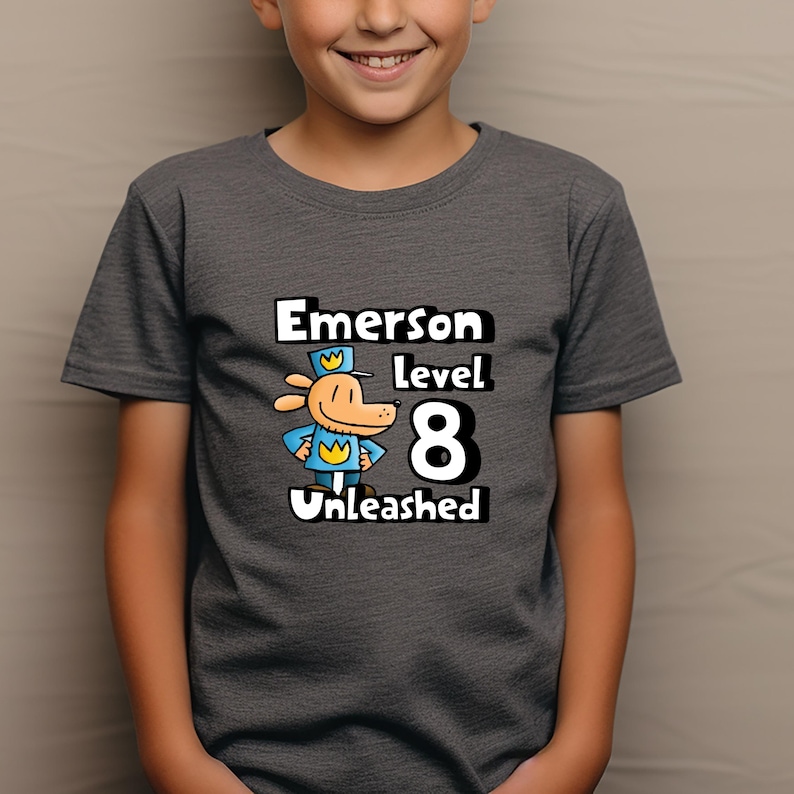May include: A dark gray t-shirt with a cartoon dog wearing a blue uniform and a yellow crown. The text "Emerson level 8 Unleashed" is printed on the shirt.