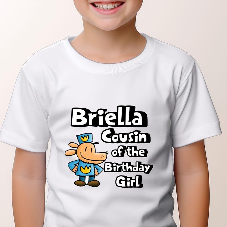 May include: White t-shirt with a cartoon dog wearing a blue uniform and a yellow crown. The text "Briella Cousin of the Birthday Girl" is printed on the shirt.