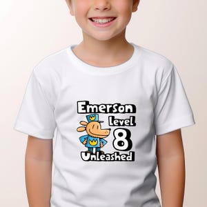 May include: White t-shirt with a cartoon dog wearing a blue hat and the text "Emerson level 8 Unleashed".