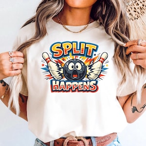 Può includere: Una maglietta color crema con una grafica a tema bowling. Il design include una palla da bowling con un'espressione sorpresa, due birilli e le parole "SPLIT HAPPENS" in un carattere audace e colorato. La maglietta è realizzata in materiale morbido.